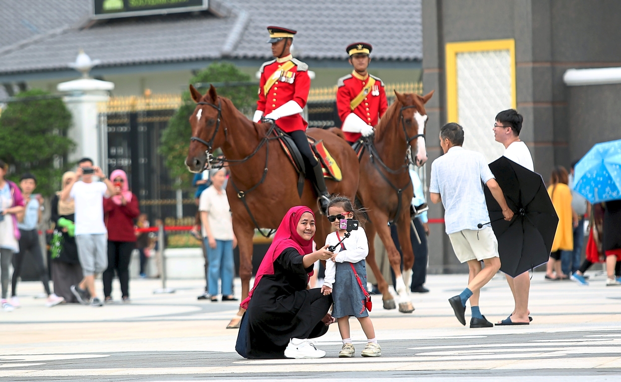 One for the album: a woman taking a wefie with her daughter as palace guards monitor the crowd outside Istana Negara.