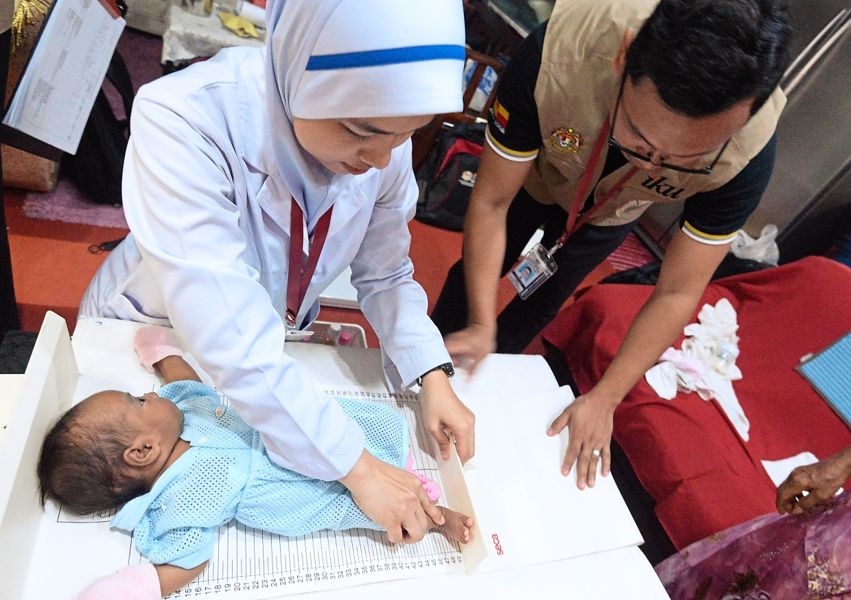 Nurse Nur Syakira Hazwani Mohamad Rudian (left) and trained interviewer Syed Mohammad Iqbal Syed Mazlan checking the vital statistics of a baby in one of the houses visited during the national survey that involves about 12,000 households.