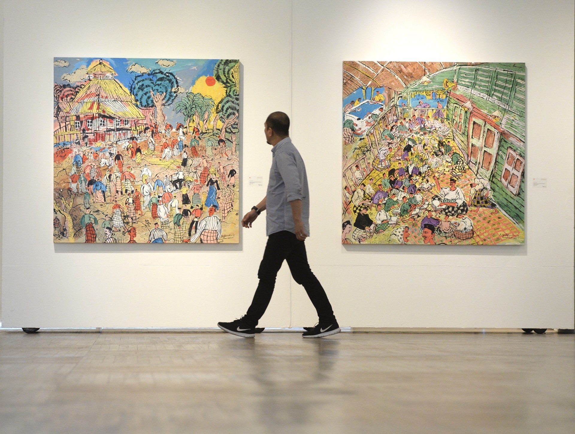 A visitors walks past Kide Baharudin's 'Jemaah Ulu Bernam - Masjid Sheikh Ismail Ulu Bernam (Masjid Tua Ulu Bernam)' and 'Mengaji Di Serambi - Masjid Sheikh Ismail Ulu Bernam (Masjid Tua Ulu Bernam)' (acrylic on canvas, 2019). Photo: The Star/Ong Soon Hin