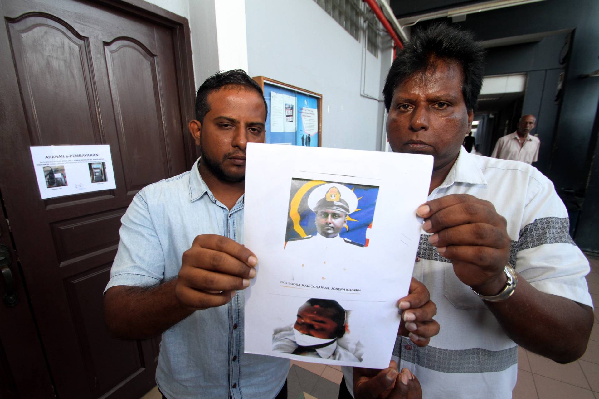 Joseph (right) and Charles (left) holding his brother's mugshot at the inquest trial of a navy cadet death at Lumut Naval Base.