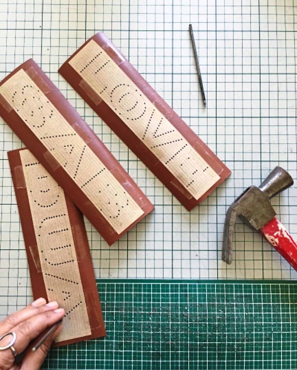A puncher and hammer are used to create the alphabets on the spine of a book.