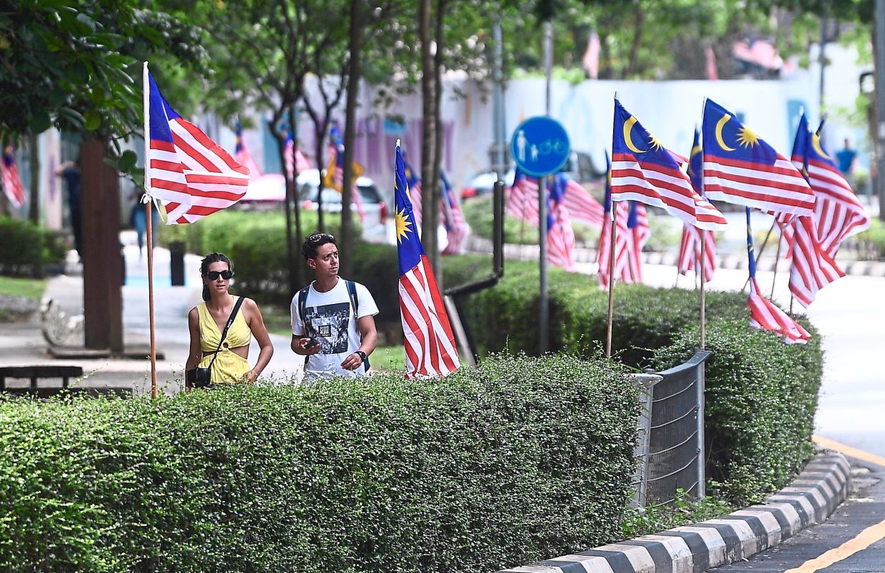 Steady momentum: People walk pass a row of flags installed in conjunction with the coming 65th Independence Day celebration in Kuala Lumpur. The post-lockdown recovery has picked up pace very well, even as the government unwinds its fiscal stimulus and certain subsidy measures. — Bernama