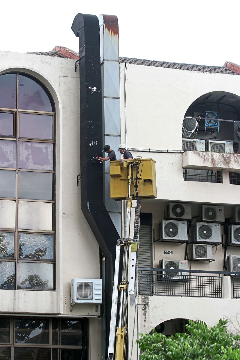 A DBKL officer using a crane to remove a giant exhaust fan that was illegally put up by a business.