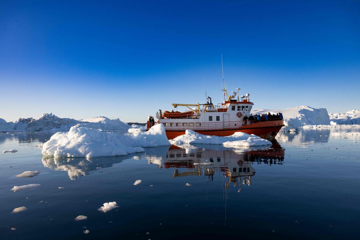 A boat carrying tourists manoeuvres among icebergs floating in Disko Bay, Ilulissat, western Greenland. – Photo: AFP