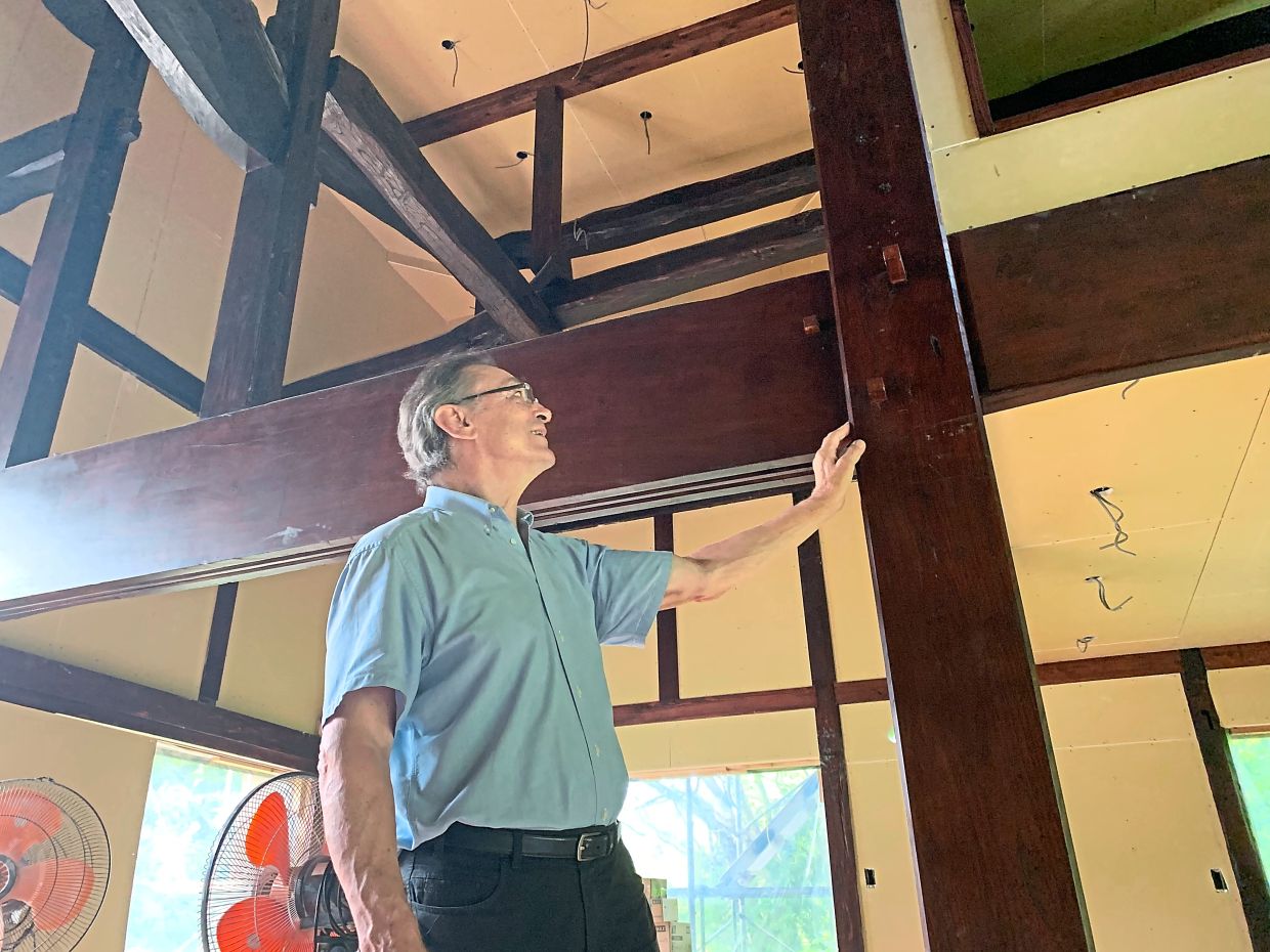 Bengs standing next to support beams from an old kominka which he is using to build a new house for a client. The beams are inserted into each other according to a traditional building method, without the need for nails or screws. 