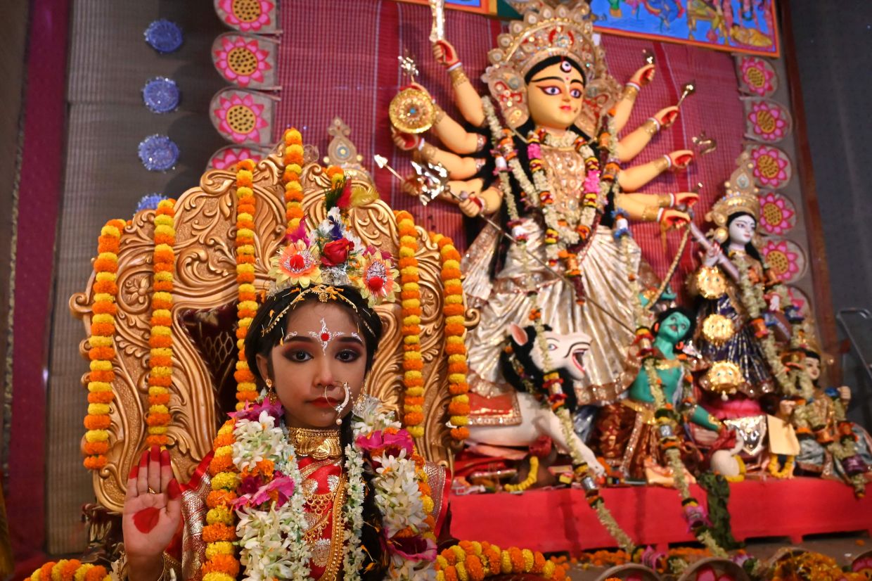 A young girl worshipped as an incarnation of Goddess Durga, sits next to the idol of Hindu Goddess Durga at a pandal during the Durga Pooja festival in Kolkata on Tuesday, October 4, 2022. - AFP