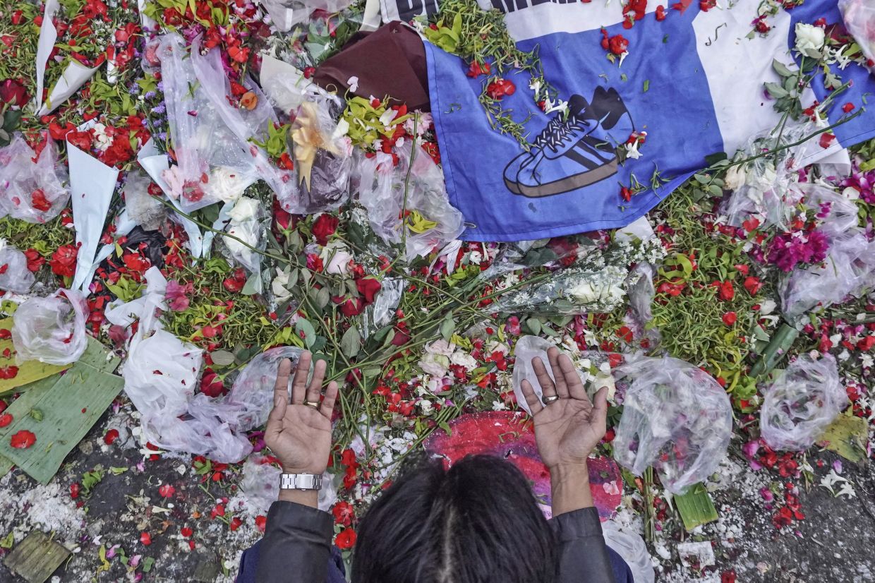 A man prays near flowers laid at the Kanjuruhan Stadium where a soccer stampede killed more than 100 people on Oct. 1, in Malang, East Java, Indonesia, Saturday, Oct. 8, 2022. Indonesia's president said the country will not face sanctions from soccer's world governing body and will remain the host of next year's U-20 World Cup after the firing of tear gas after a match inside the half-locked stadium caused the deadly crush at the exits. - AP