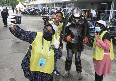 SPR officers talking a selfie with a mystery voter dress up in a Predator costume at the Desa Intan 7A polling centre in Farlim, Penang. — K.T.GOH/The Star