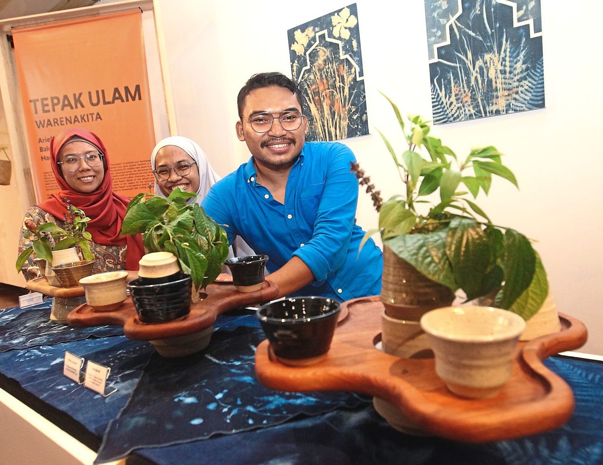 Balqis flanked by Arief and Hanisah showing the Tepak Ulam, which consists of a base cloth, ceramic containers and a wooden plate.