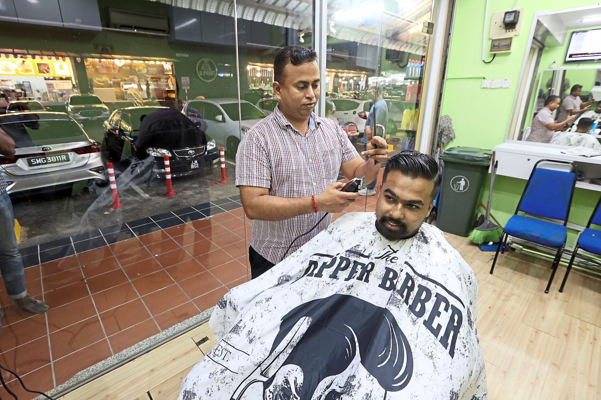 Barber Ramesh, 39, attending to a late-night customer at his shop.