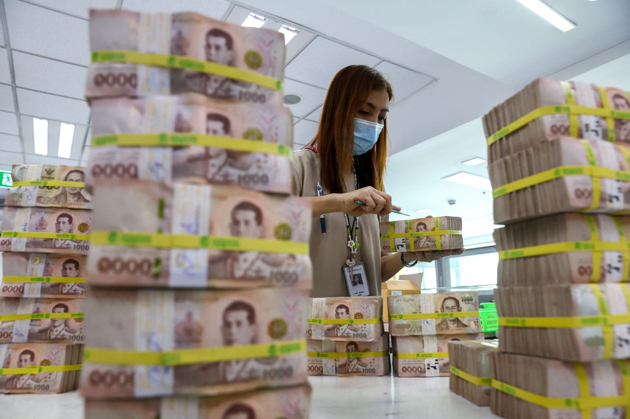 A bank employee gathers Thai baht notes at a Kasikornbank in Bangkok, Thailand. - Reuters