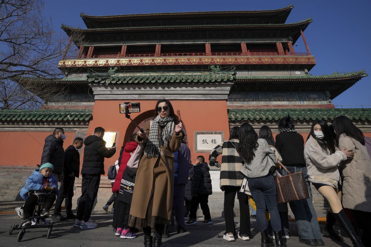 A woman takes a selfie with a sugar-coated Chinese haw as visitors gather outside the Drum Tower in Beijing. Chinese people are enjoying the Lunar New Year and visiting various tourist sites in cities around China following the lifting last month of draconian Covid-19 restrictions, allowing a return to many aspects of normal life. - AP