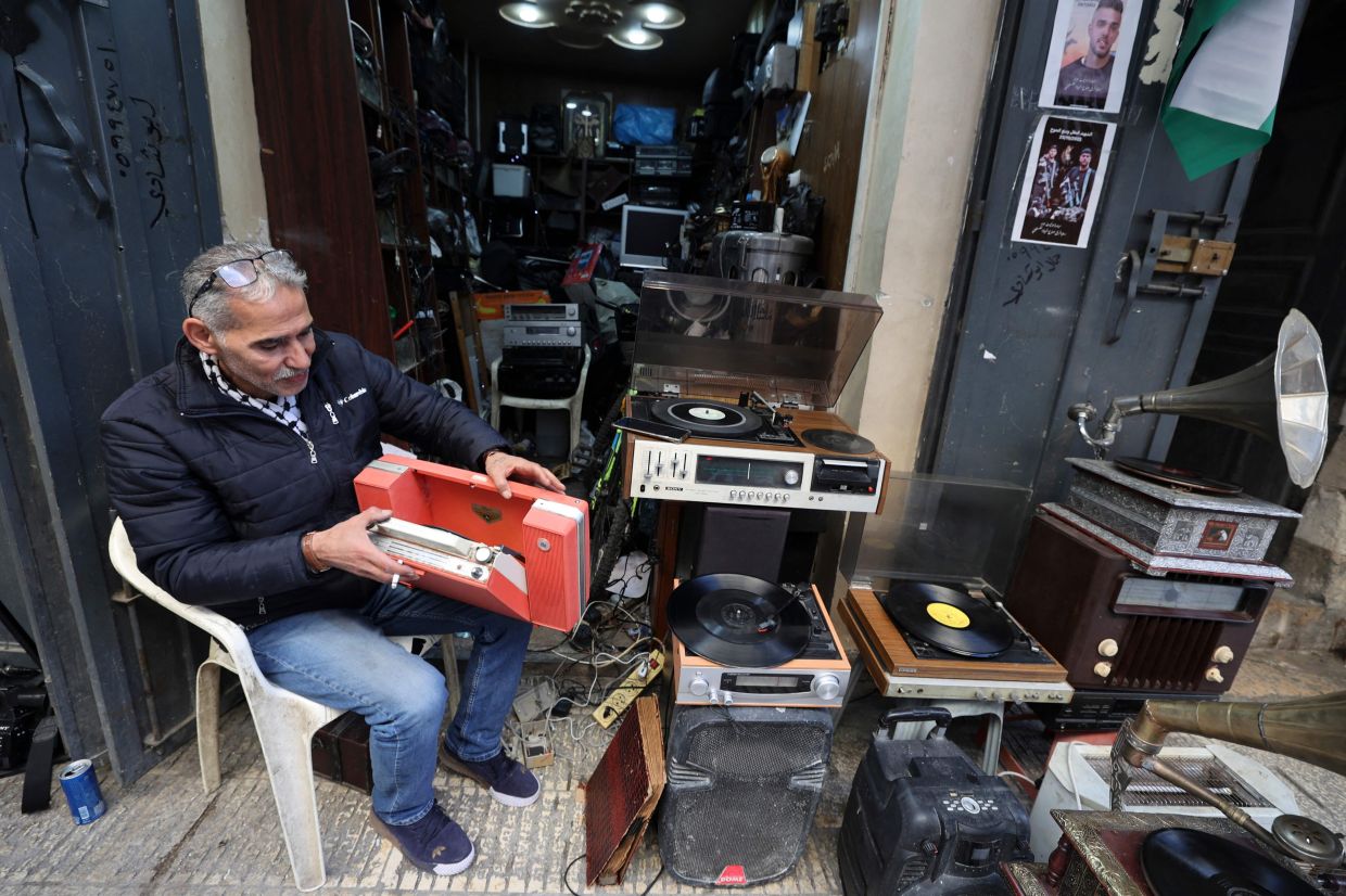 Hemmou checks a portable record player as he sits in front of his shop. Photo: AFP