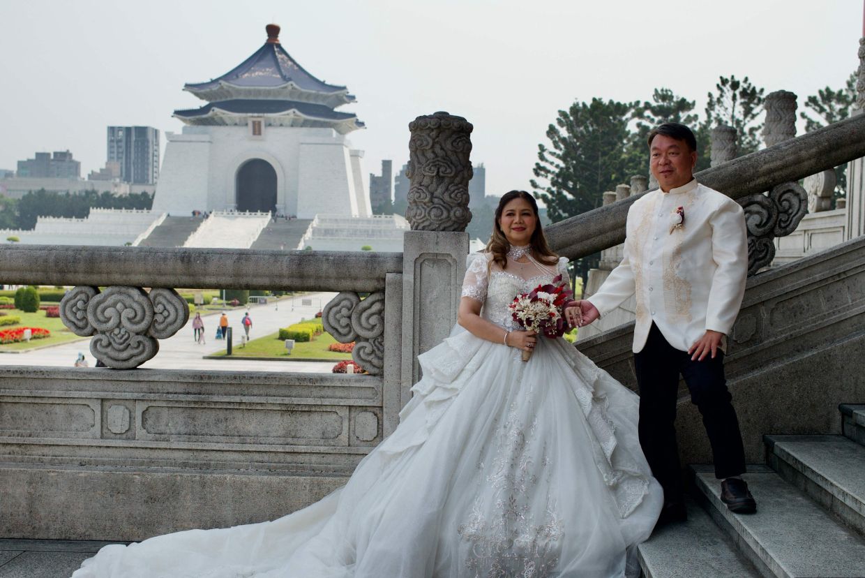 A newly-wedded couple from the Philippines pose for photos in front of the Chiang Kai-shek Memorial Hall in Taipei. - AFP