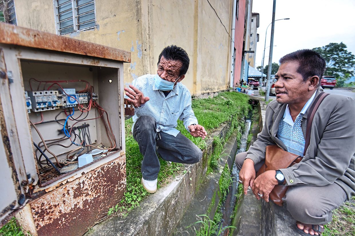 Mohd Arif (left) and another resident showing a cable that has been vandalised in Saujana Mawar.