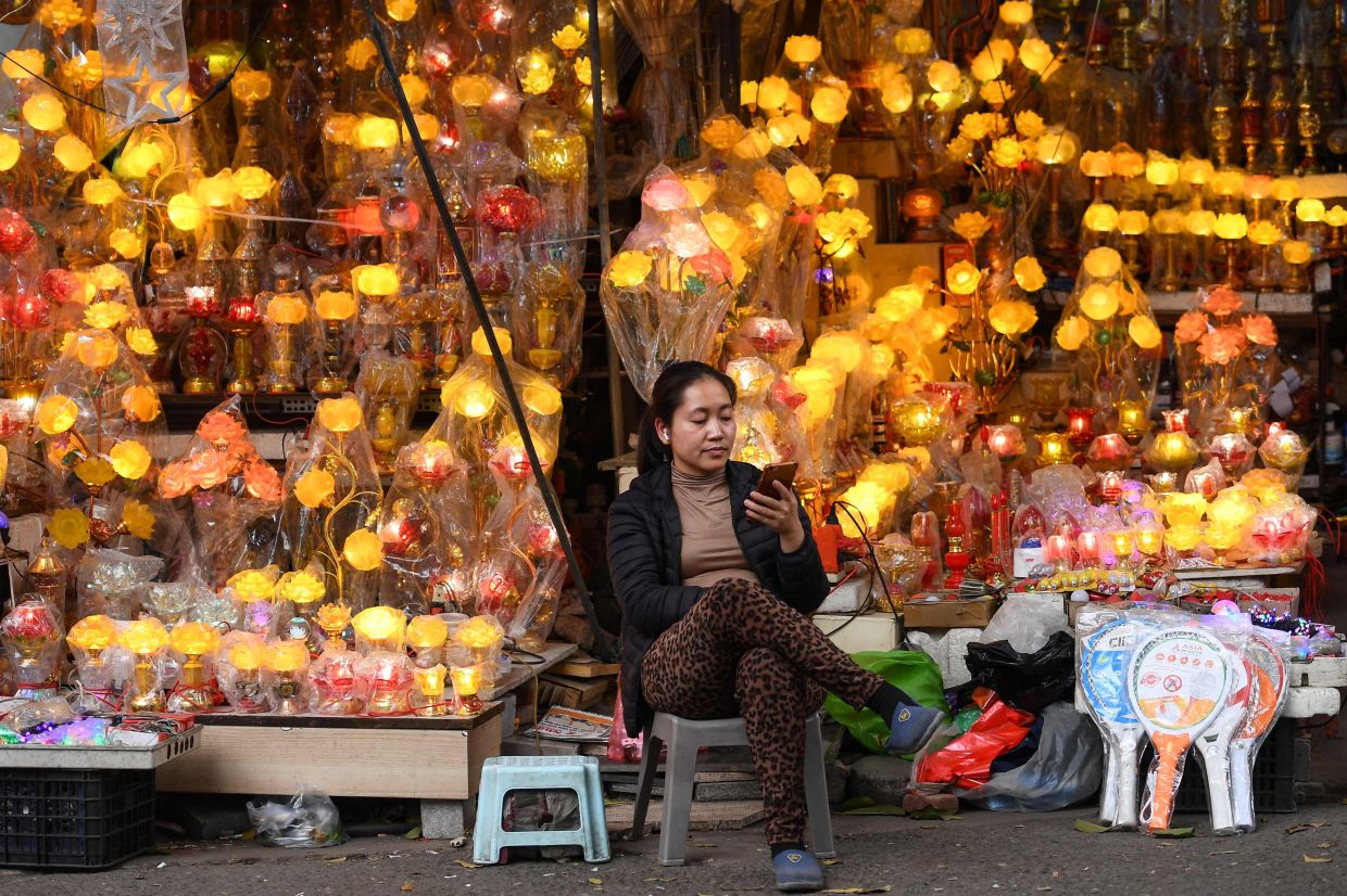 A vendors looks at her phone as she waits for customers at a lamp shop in Hanoi. - AFP