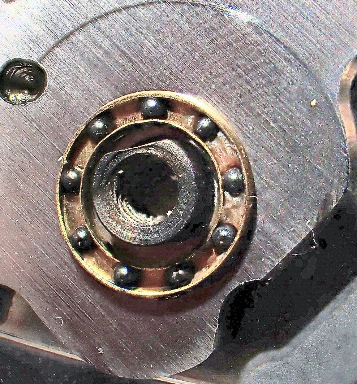 Close-up of ball bearings in a brass cage at a folding knife’s pivot. Notice the presence of grease in the brass cage, and even lint. Too much lint and the knife’s operation become affected.
