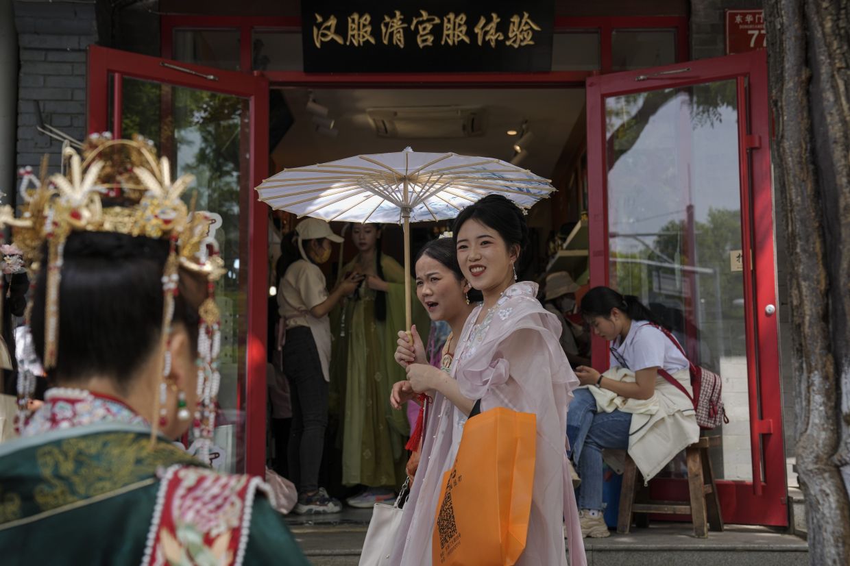 Women dressed in traditional costumes walk by vendors attend visitors at a shop renting traditional costumes near the Forbidden City during the May Day holiday period in Beijing, Tuesday, May 2, 2023. - AP