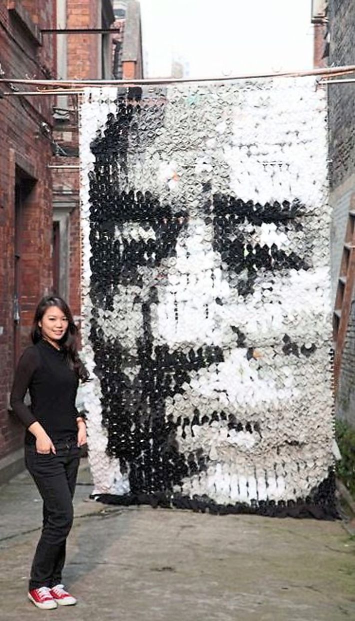 Red standing in front of the giant portrait of Zhang Yimou, an artwork created in 2012 with socks and pins hung off bamboo sticks in an alleyway in Shanghai.