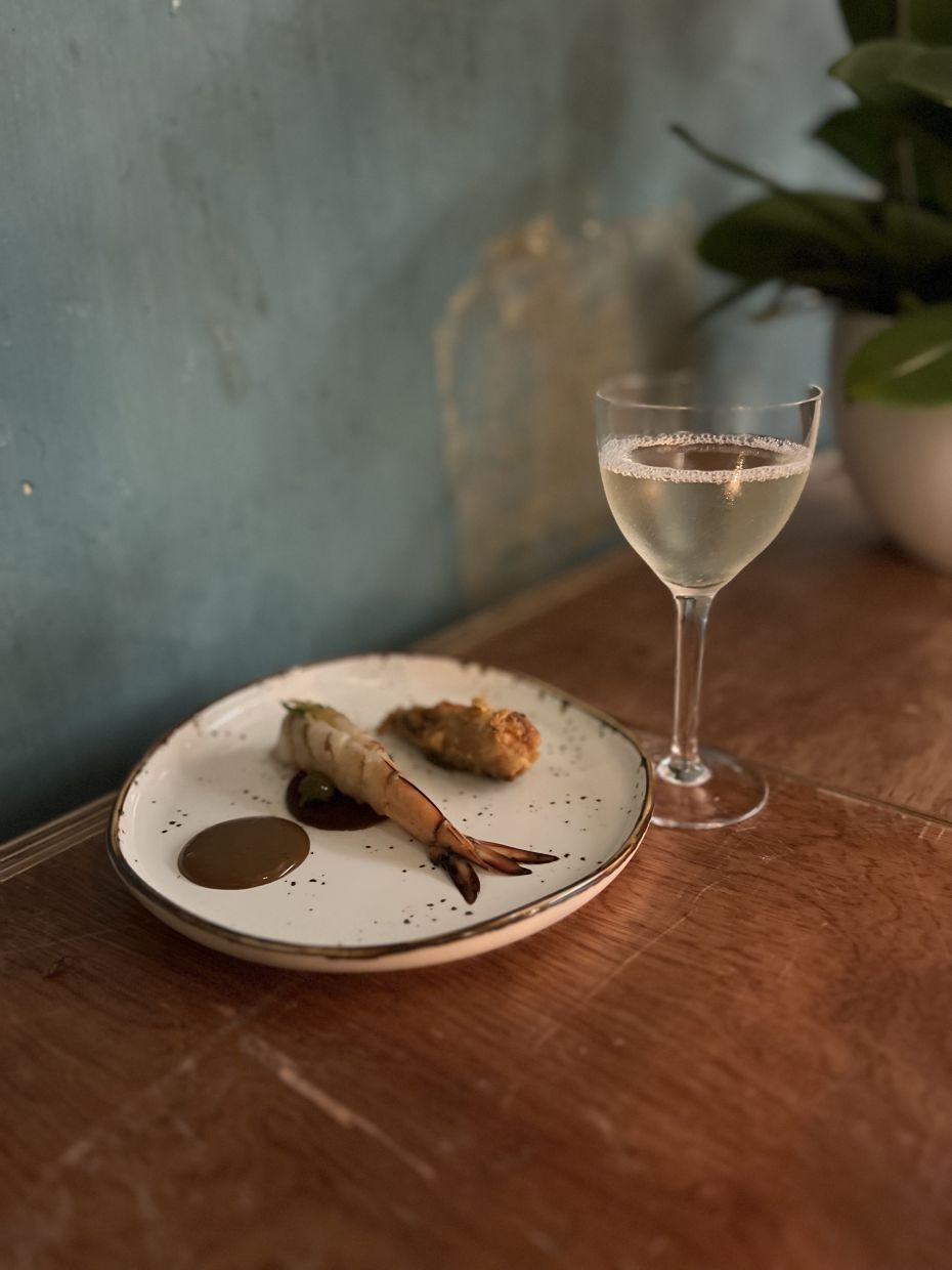King prawn served with black garlic emulsion and seafood gel and marigold leaf, paired with a cocktail made with shochu, salted mandarin, and orange bitters.