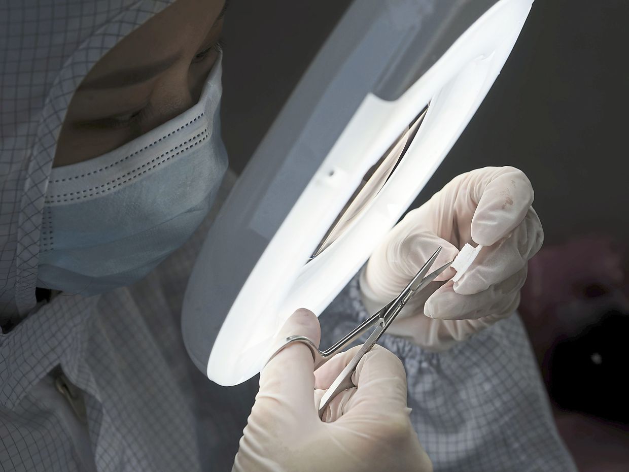 A production operator inspecting a 3D printed device under magnification.