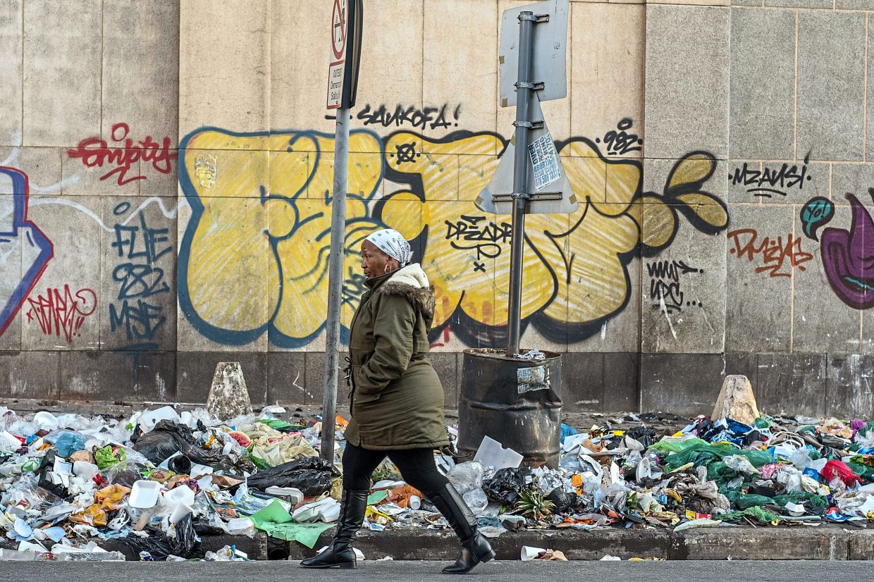 A woman walking past uncollected trash in the city. — The New York Times