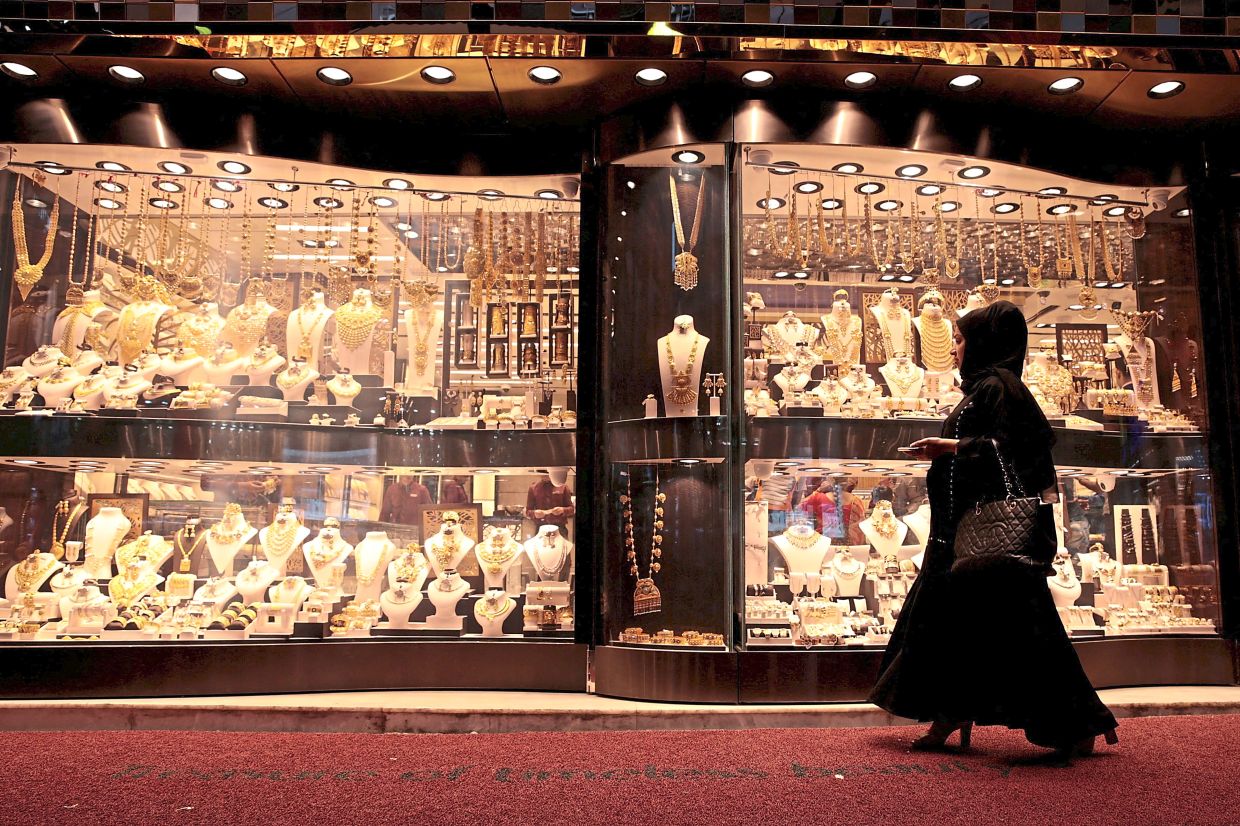 A woman walking past gold jewellery displayed in a shop window at the Gold Souq in Dubai, United Arab Emirates. — Reuters