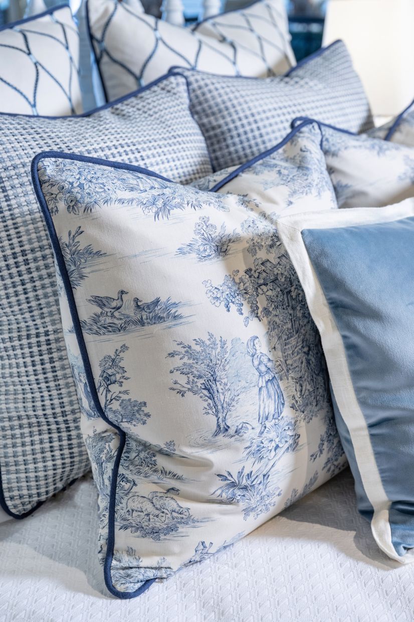 The pillows on this bedscape mix blue and white toile with similarly coloured woven, embroidered, and velvet fabrics.