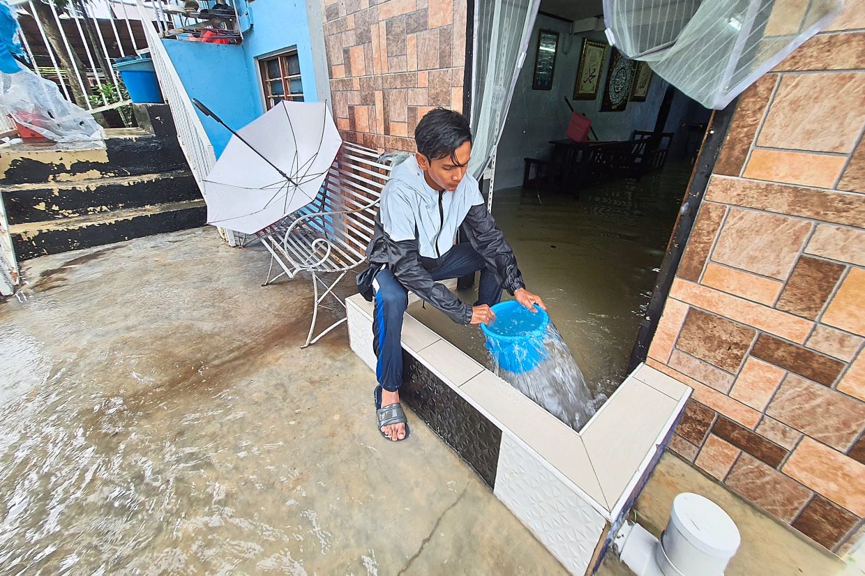 Water damage:  Sahar Shamsudin, 29, scooping out floodwater from the compound of his house with a bucket in Jalan P. Ramlee in Taman P. Ramlee. — CHAN BOON KAI/The Star