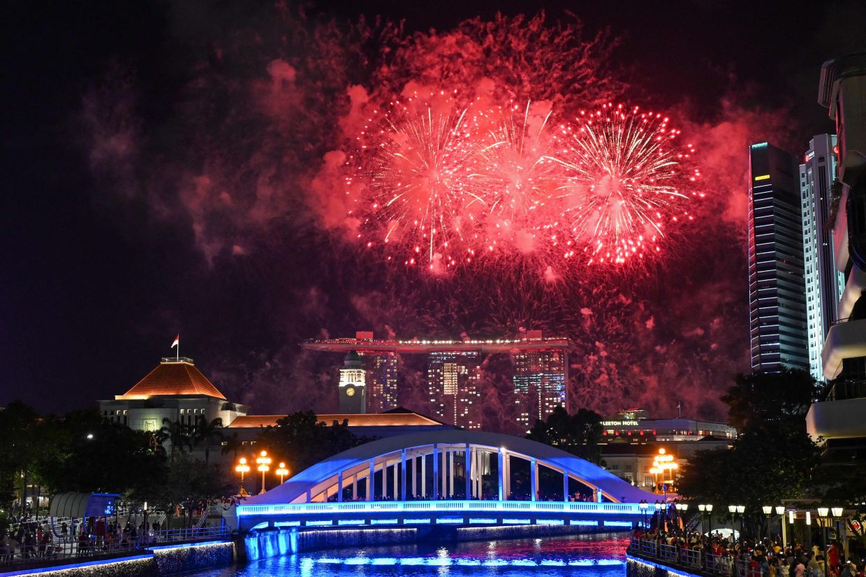 People watch fireworks illuminate the city skyline during the country's 58th National Day celebrations in Singapore. - AFP