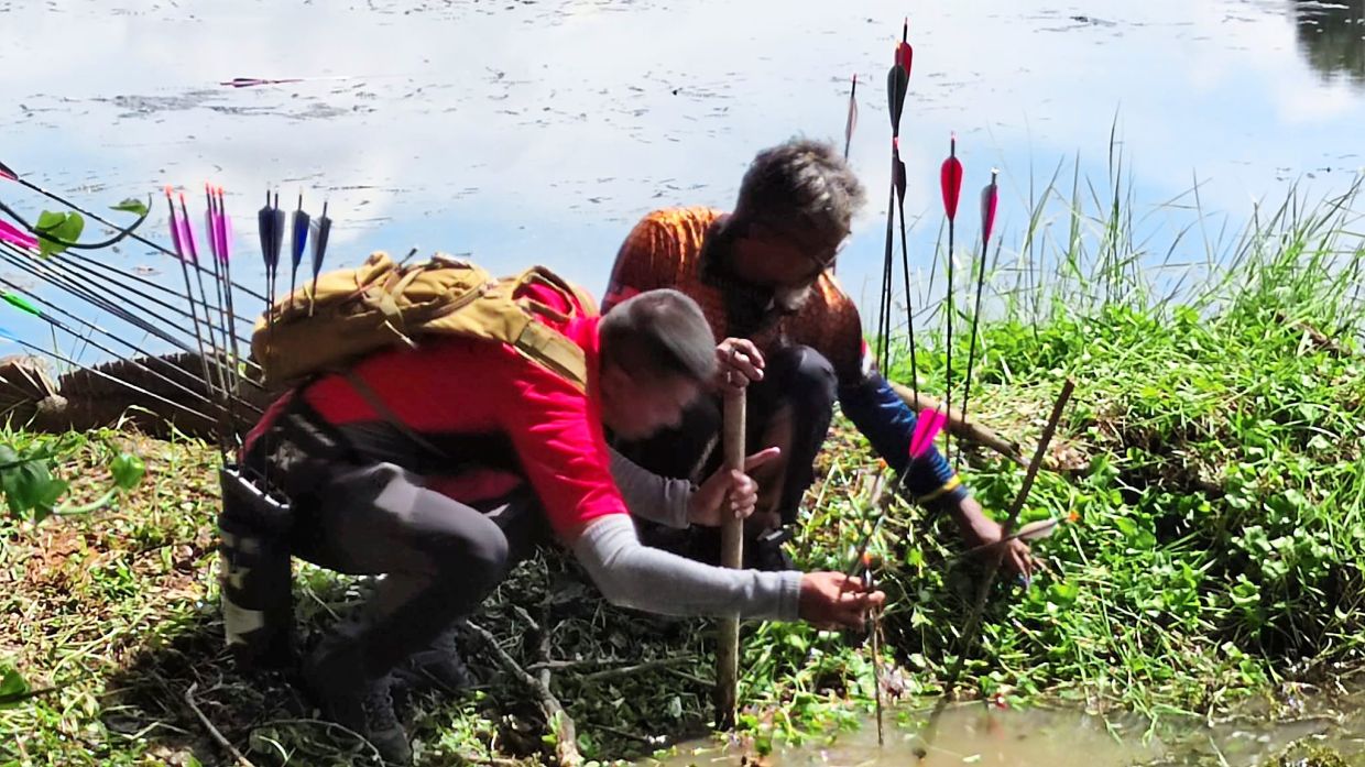 Archers searching for stray arrows near a lakeside.