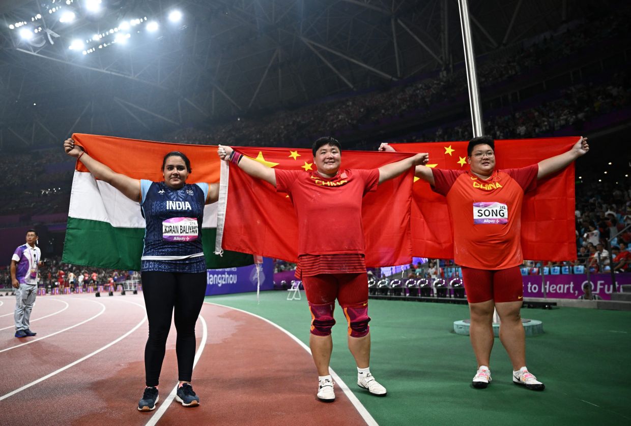 India's Kiran Baliyan holds the Indian flag (left), with China's Lijiao Gong and Jiayuan Song, who hold the Chinese flags after the Women's Shot Put Final at the Olympic Sports Centre Stadium, Hangzhou, China on Friday, Septe29, 2023. - AFP