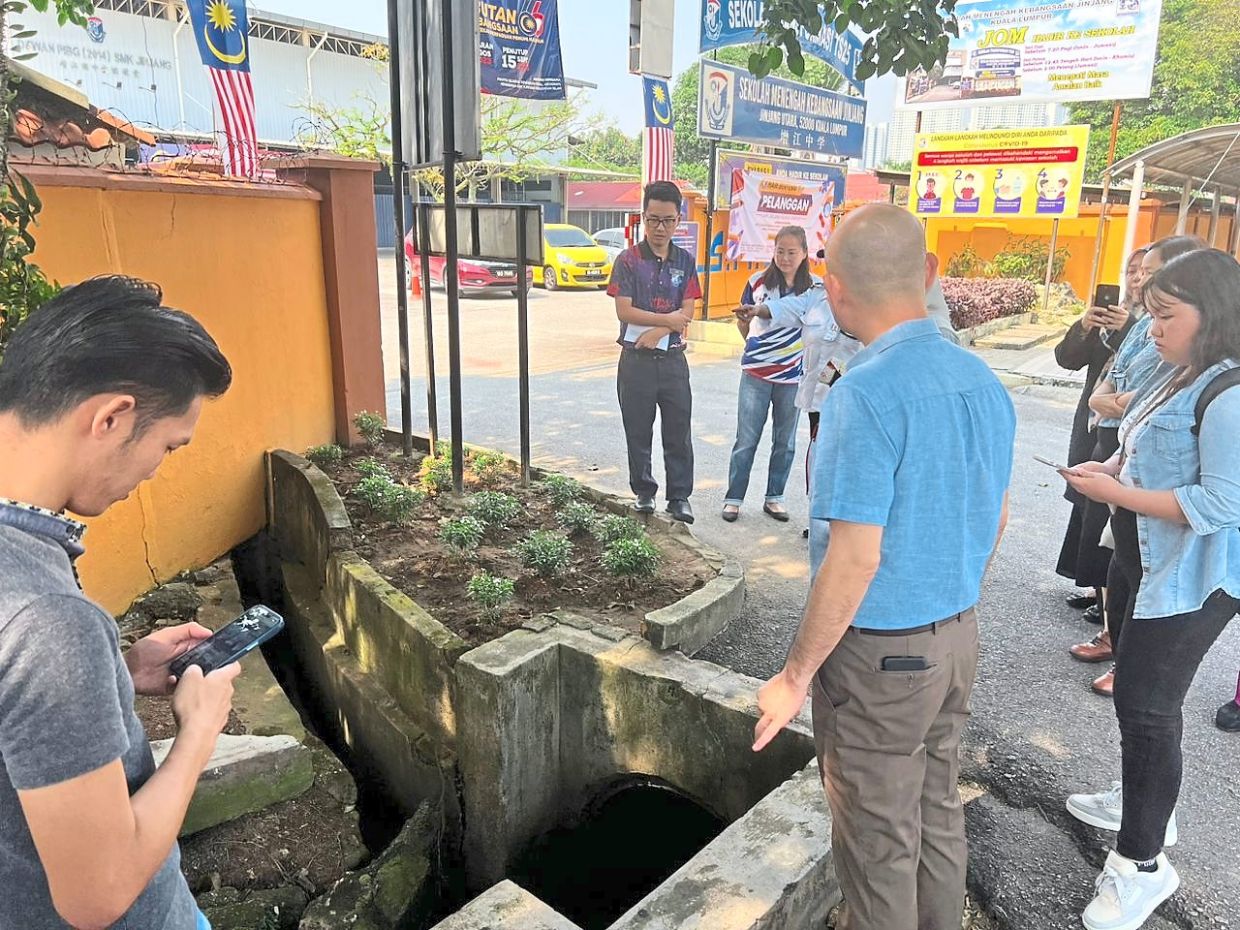 Lim (in blue) inspecting the clogged drain outside SMK Jinjang. 