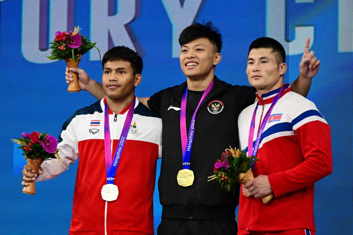 Gold medallist Indonesia’s Rahmat Abdullah (centre), bronze medallist North Korea’s OH Kumthaek and Thailand’s silver medallist Weeraphon Wichuma (left) stand in the podium during the medal ceremony for the men’s 73kg group A weightlifting competition during the 2022 Asian Games in Hangzhou, in China's eastern Zhejiang province on October 3, 2023. - AFP