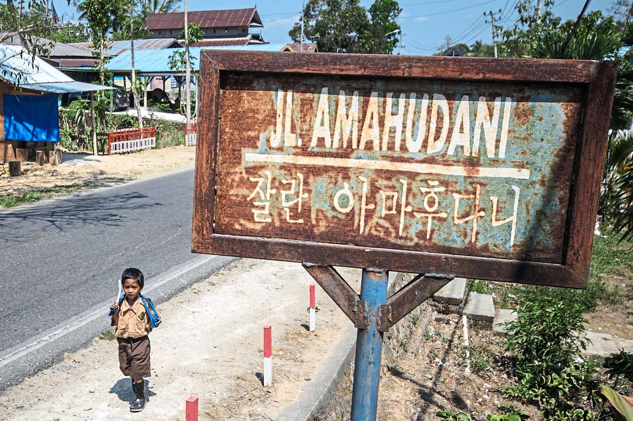 A student walking past a signboard which shows the name of the road in Indonesian and Hangul. — AFP