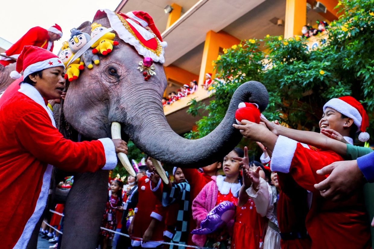 Students wait for gifts from an elephant dressed in a Santa Claus costume ahead of Christmas celebrations at a school, in Ayutthaya, Thailand. - Reuters