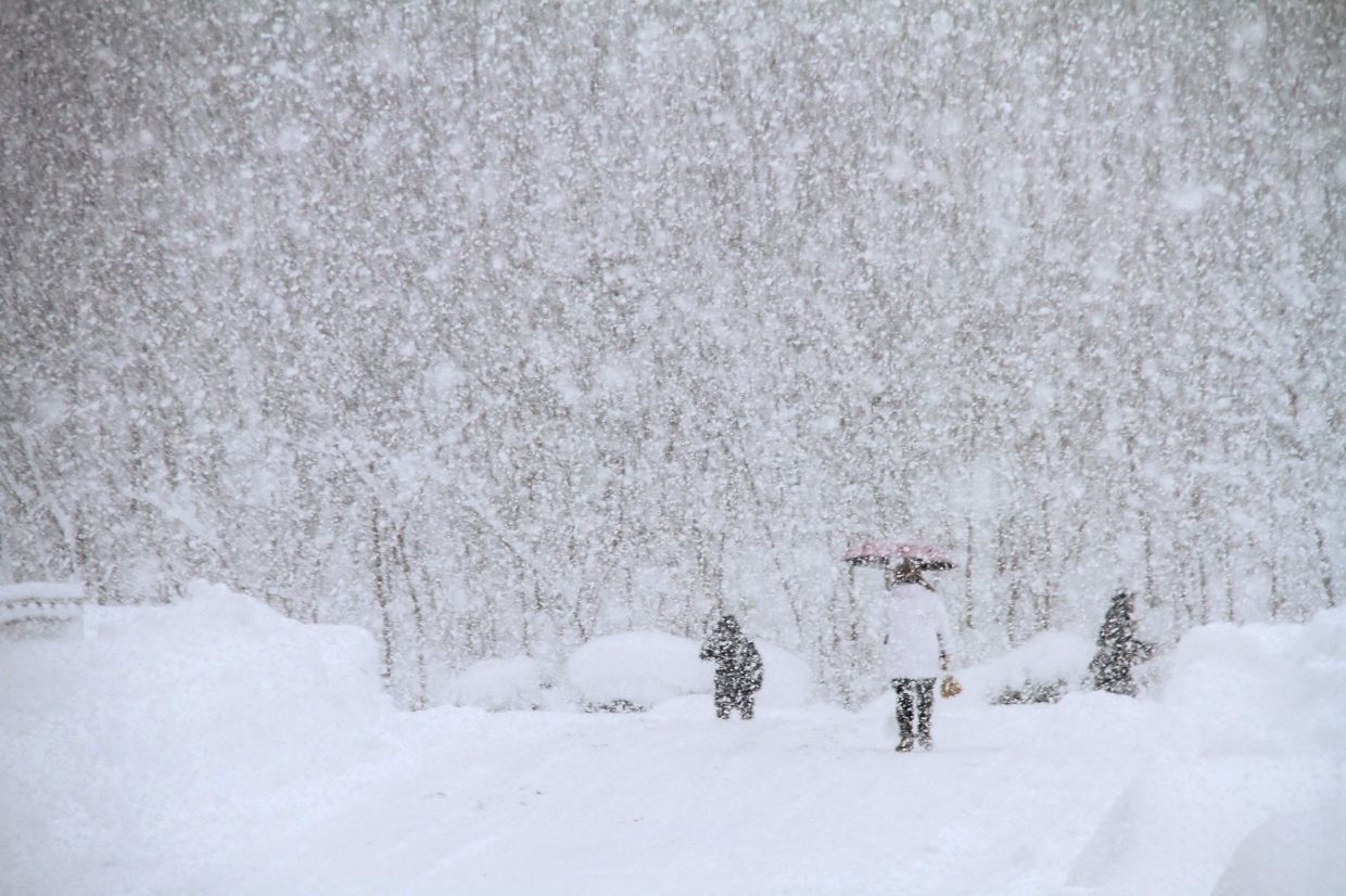 People walk on a street during heavy snowfall in Weihai, in Chinas eastern Shandong province. - AFP