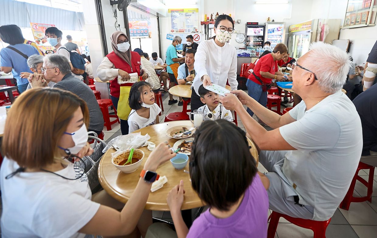 Tan distributing face masks at a coffeeshop. — Photos: ZHAFARAN NASIB/The Star