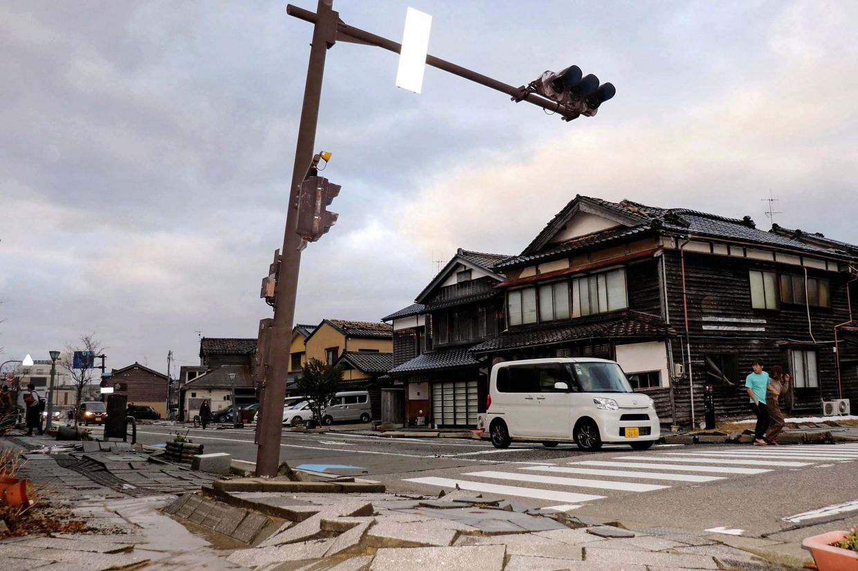 A car drives past a badly damaged pavement along a street in the city of Wajima, Ishikawa prefecture on January 1, 2024, after a major 7.5 magnitude earthquake struck the Noto region in Ishikawa prefecture in the afternoon. Tsunami waves over a metre high hit central Japan on January 1 after a series of powerful earthquakes that damaged homes, closed highways and prompted authorities to urge people to run to higher ground. - AFP