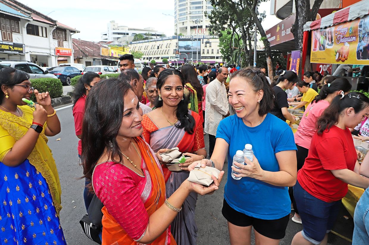 Always there for each other: Quennie Teoh (in blue T-shirt) helping to distribute food packets and drinks to devotees participating in the Thaipusam celebration along Jalan Keramat, George Town. — LIM BENG TATT/The Star