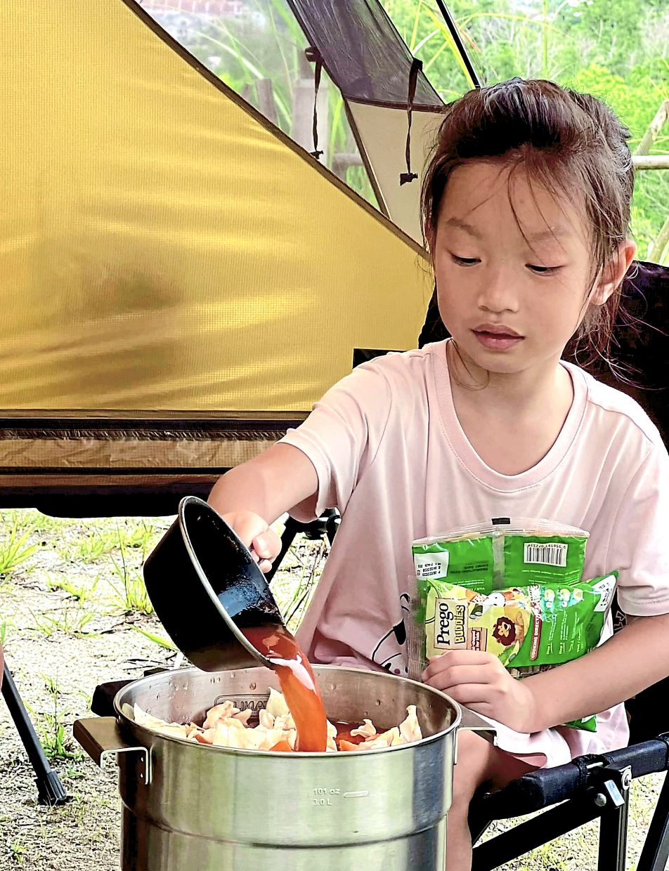 Avryl adding a swirl of water and tomato puree into a pot of minestrone soup.
