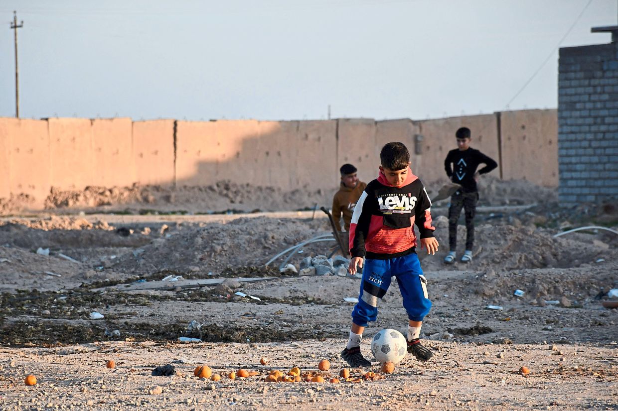 Iraqi children playing football in front of a section of the Samarra Wall in the city of Samarra. — AFP