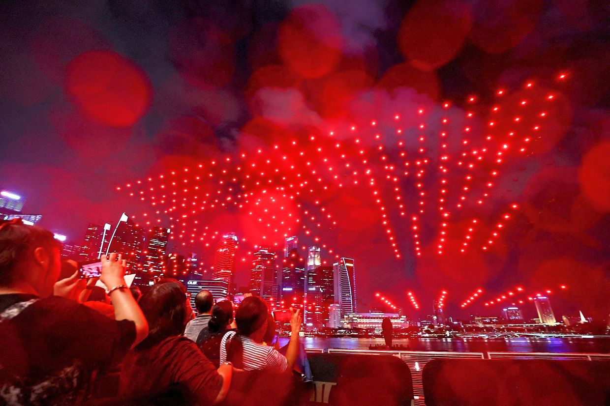 Dazzling drones: Visitors taking pictures of the city skyline lit up by drones during a performance to welcome the Lunar New Year at Marina Bay in Singapore.— Reuters
