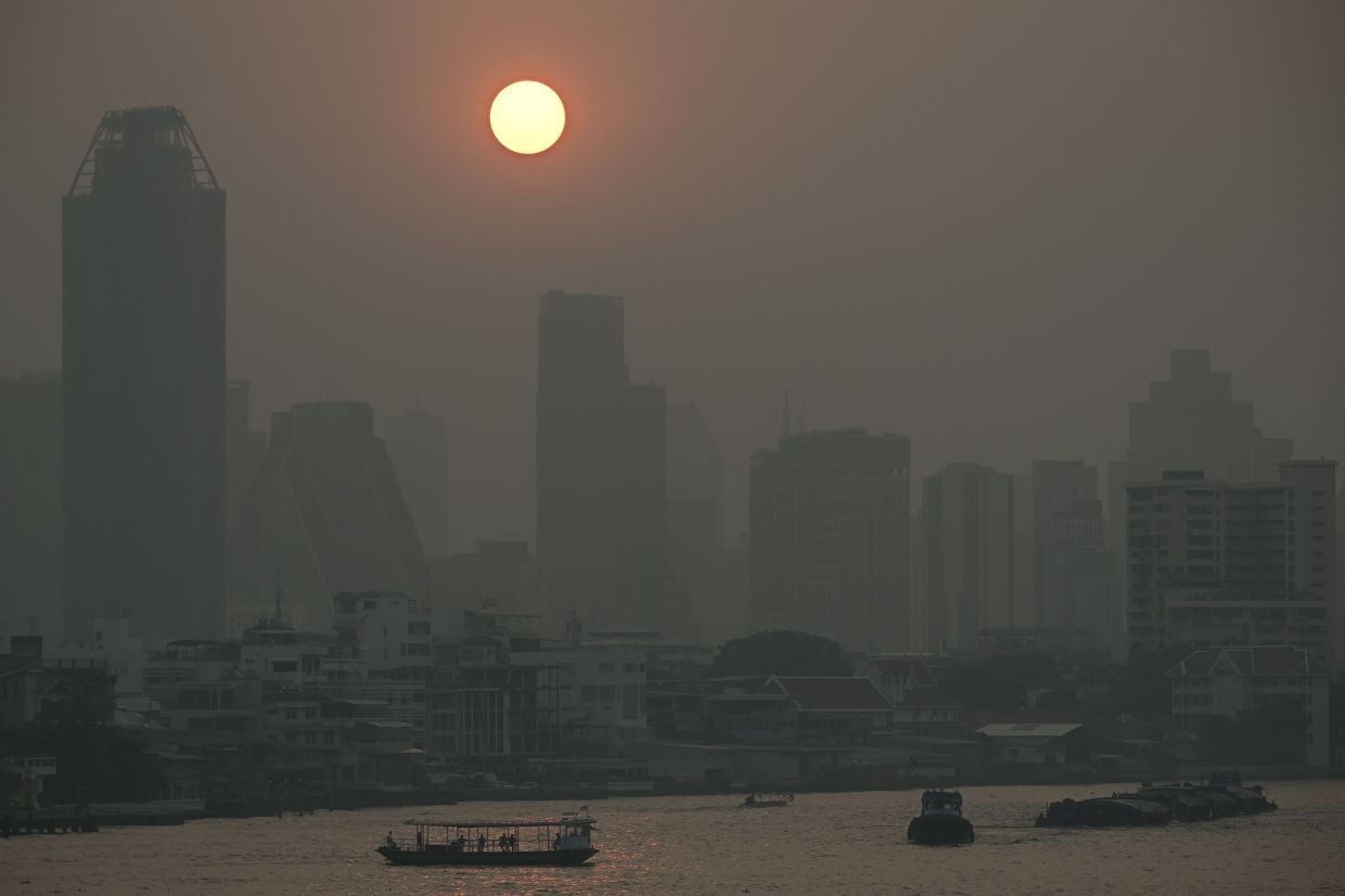 Commuter boats cross the Chao Praya River amid high air pollution levels in Bangkok over the last few days. - AFP
