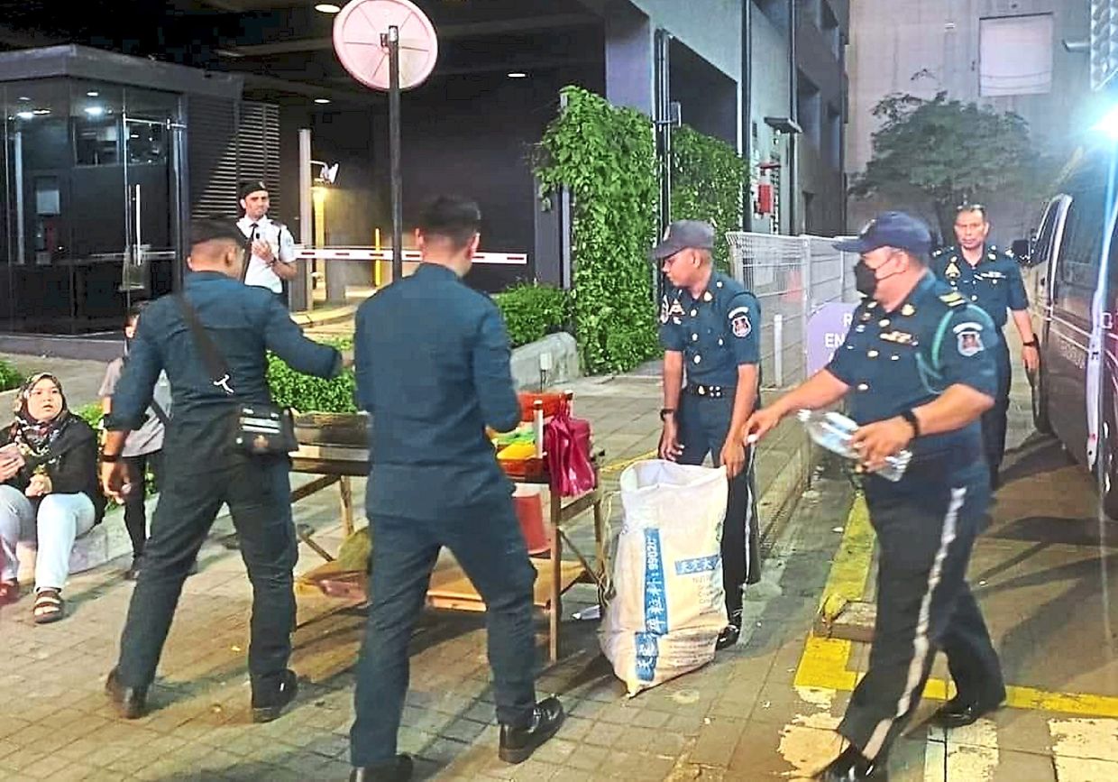 DBKL enforcement officers removing equipment of roadside stalls set up next to a zebra crossing.