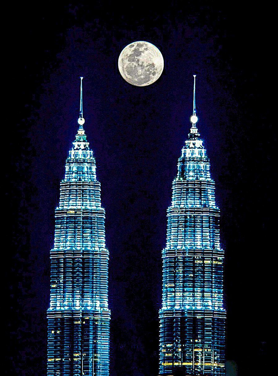 The symmetry of the PETRONAS Twin Towers creates a visually harmonious effect against the backdrop of the ascending moon.