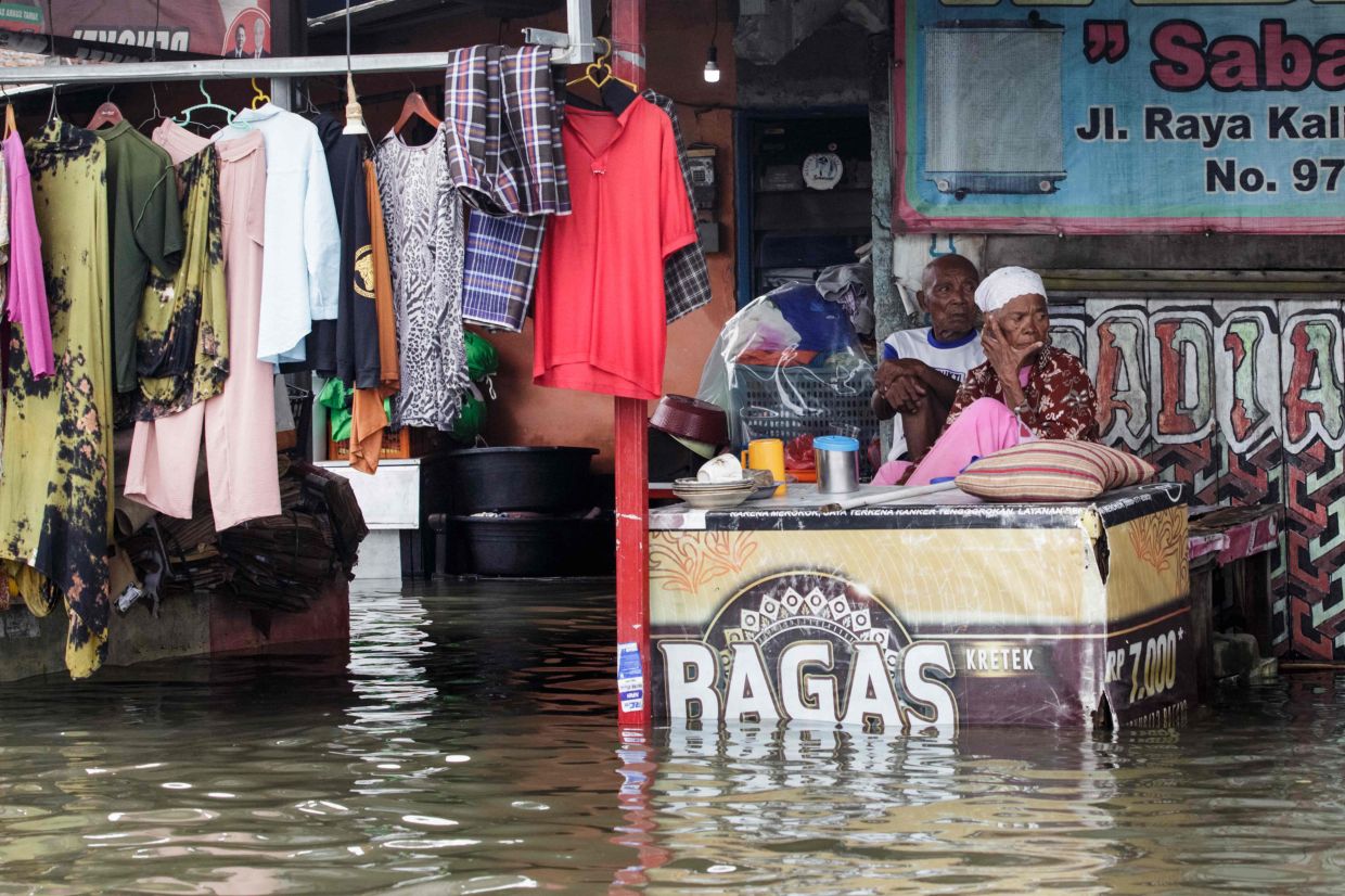 Elderly people rest on a table in flooded water after the heavy rain in Semarang, Central Java, on Friday, March 15, 2024. - AFP