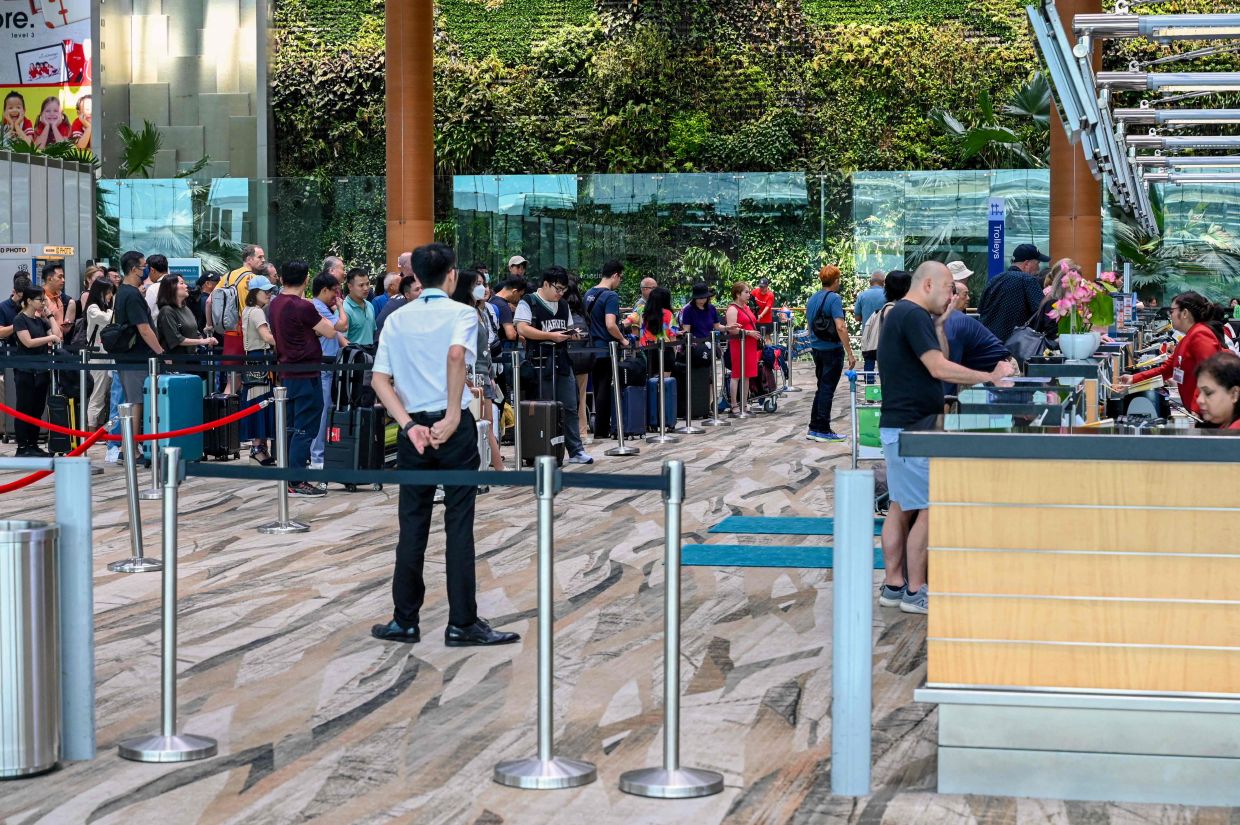 Passengers queue at the check-in departure counter at Singapore Changi Airport in Singapore. - AFP