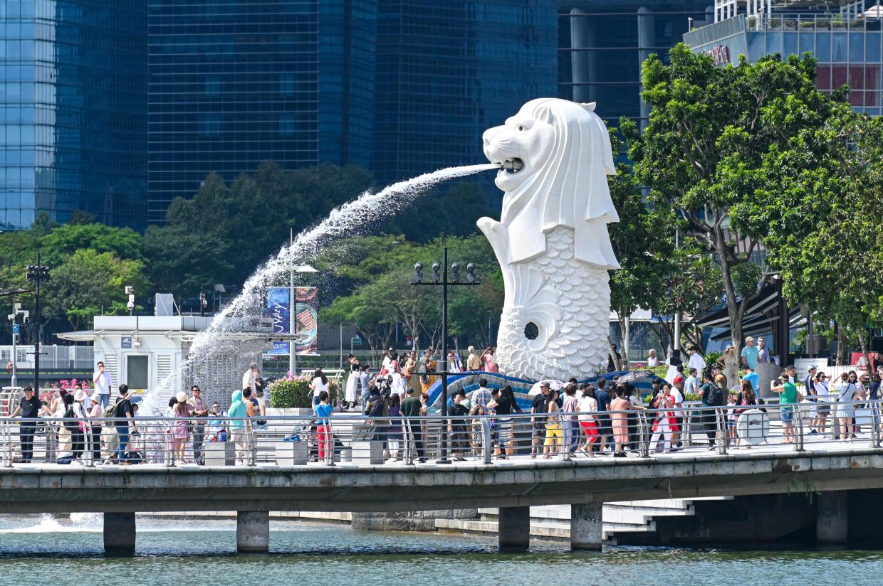 People gather for photograph next to the Merlion statue at Marina bay waterfront in Singapore on Monday, March 18, 2024. - AFP