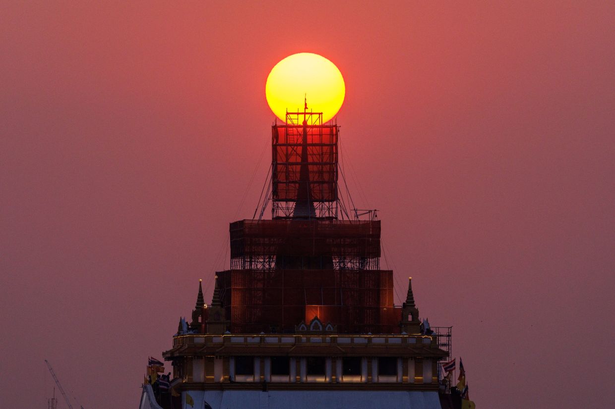 The sun sets behind the Wat Saket Temple's Golden Mount, which is undergoing renovation, in Bangkok, Thailand, Monday, March 18, 2024. - Reuters